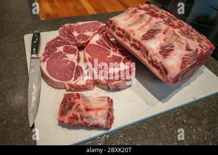 Roh-Rindfleisch Prime Rib Braten und Steaks mit dicken Fleischstücken, die Marmorierung von Fett und Rippenknochen. Das Fleisch sitzt auf einem weißen Schneidebrett. Stockfoto