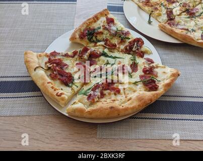 Pizza mit Prosciutto, heißem Käse und Rucola-Salatblättern, in Scheiben geschnitten auf dem Teller serviert Stockfoto