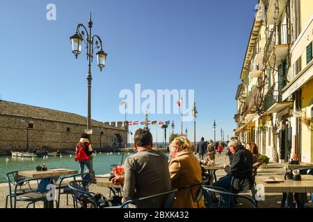 Leute genießen den Aperitif am Ufer der Altstadt am Ufer des Gardasees mit dem Kanal und der Dogana Veneta, Lazise, Verona, Italien Stockfoto