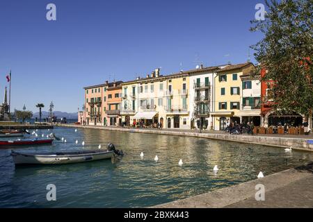 Blick auf den Hafen der Altstadt am Ufer des Gardasees mit festangetäuten Fischerbooten im Wasserkanal, Lazise, Verona, Venetien, Italien Stockfoto