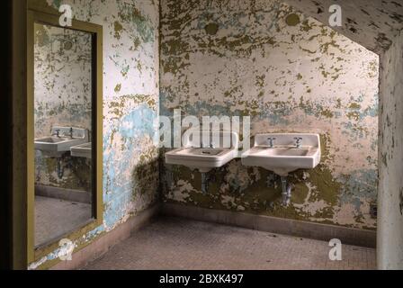 Badezimmer in einer verlassenen Asyl zeigt zwei Waschbecken in einem Spiegel reflektiert. Stockfoto