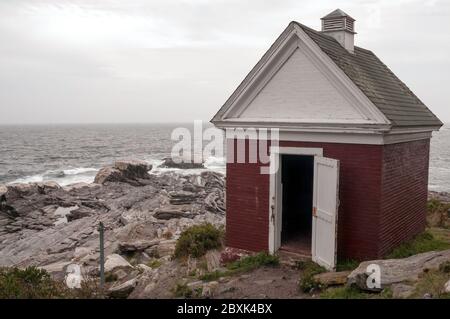 Ölschuppen, verwendet für die Lagerung von Leuchtturmöl, auf den Felsen sitzend mit der Meeresbrandung im Hintergrund, am Pemaquid Point Leuchtturm gelegen. Stockfoto