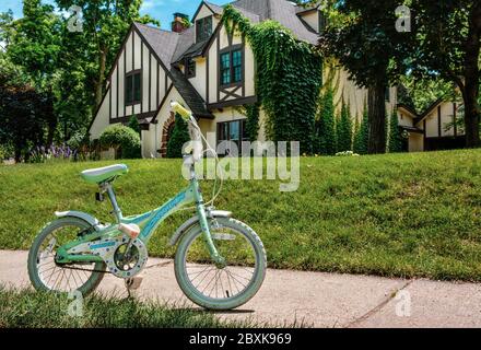 Eine klassische Szene der Americana mit Kinderfahrrad allein auf dem Bürgersteig vor dem gehobenen historischen Haus in St. Cloud, MN, USA, Stockfoto