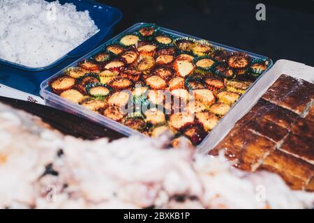 Philippinische Desserts auf dem Tisch - in voller Sicht ist der rechteckige klare Plastikbehälter aus Kokosnuss-Makronen in bunten Pappbechern. Stockfoto