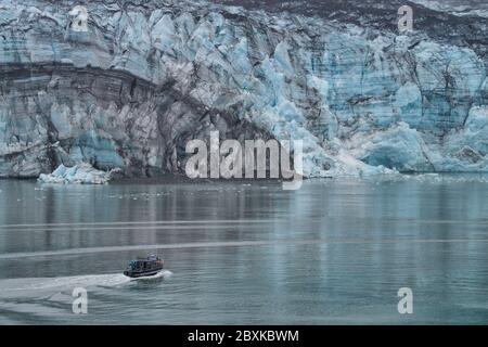 Fischerboot nähert sich Gletscher im Glacier Bay National Park in Alaska an einem regnerischen, nebligen Tag. Das kleine Boot zeigt die Größe des Gletschers. Stockfoto