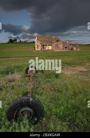 Landtechnik vor einem verlassenen Haus auf einem Feld mit Sturmwolken am Himmel. Bild aufgenommen im Palouse, Staat Washington. Stockfoto