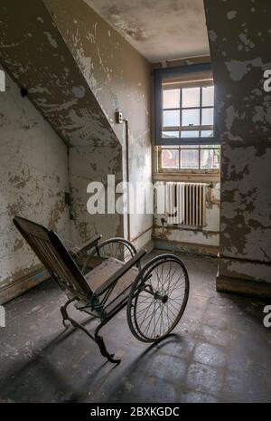 Leerer Rollstuhl mit Blick auf ein Fenster in einer verlassenen Asyl Stockfoto