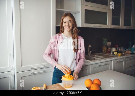 Ingwer kaukasische Dame mit Sommersprossen lächelt in der Kamera, während sie Früchte quetscht und Saft macht Stockfoto