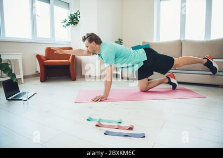 Kaukasischer Mann tun Fitness-Übungen vor einem Laptop, während mit Online-Fitness-Unterricht Stockfoto