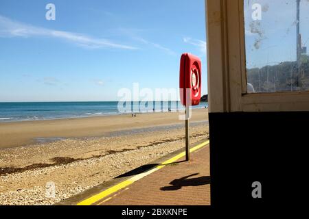 Schatten auf dem Bürgersteig der Person, die an der Strandpromenade vorbeiging Schutz und lebensrettende Ring Auftrieb Hilfe Blick über weit Sandstrand bei Ebbe Stockfoto