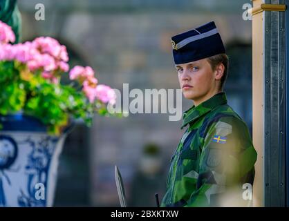 Stockholm, Schweden - 17. August 2017: Schwedische Militärs weibliche Offizierin in Tarnuniform am Wachposten des Königlichen Palastes, Blumen im Vordergrund Stockfoto