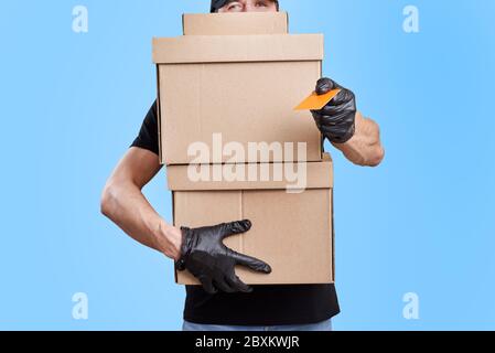 Lieferung Mann in schwarzer Uniform mit medizinischen Handschuhen und Schutzmaske halten Pappkarton. Kontaktloses Lieferdienstkonzept Stockfoto