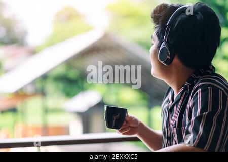 Ein Asiat hört Musik mit Kopfhörern, während er Kaffee trinkt Stockfoto