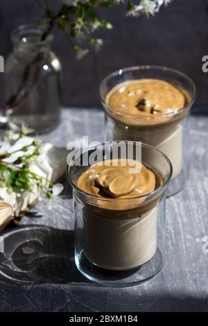 Dalgona Kaffee in transparenten Gläsern und ein Buch auf einem sonnenbeschienenen Tisch. Stockfoto