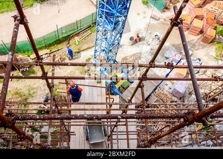 Das Gerüst wird gegen das Gebäude gestellt. Chef wird von der Holzplattform über der Baustelle beaufsichtigt. Stockfoto