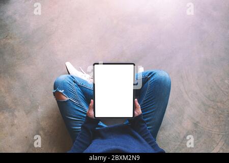 Draufsicht Mockup-Bild einer Frau mit schwarzen Tablet-pc mit leeren weißen Bildschirm, während auf dem Boden sitzen Stockfoto