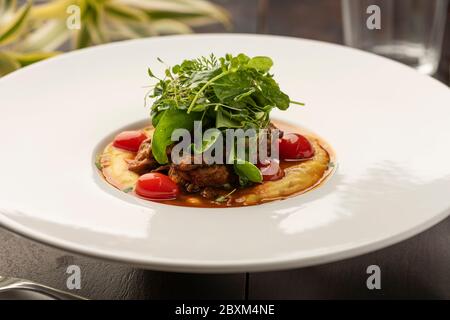 Cremige Polenta mit Maismehl mit confit Tomaten und Salat mit verschwommenem Hintergrund Stockfoto