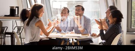 Multiethnische Mitarbeiter versammelten sich in der Büroküche und lachten beim Pizzaessen Stockfoto