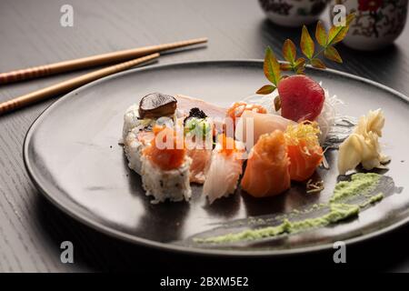 Sushi Sashimi niguiri Wasabi auf dunklem Keramikplatte Essstäbchen und Tassen auf schwarzem Holztisch Stockfoto