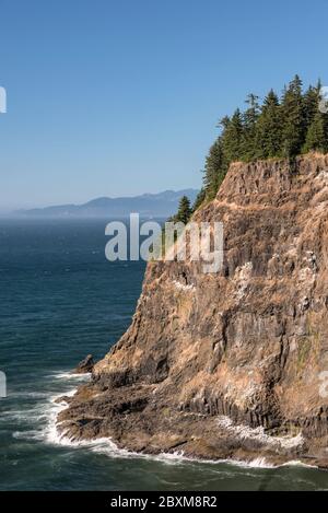 Steile Klippe an der Küste von Oregon, umgeben von Wellen mit Nebel im Hintergrund. Stockfoto