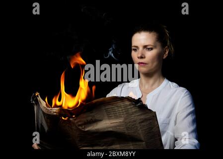 Eine Frau hält eine brennende Zeitung. Fake News Konzept. Soft Focus. Stockfoto