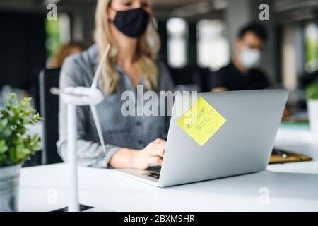 Unerkennbare junge Frau mit Gesichtsmaske zurück bei der Arbeit im Büro nach Lockdown. Stockfoto