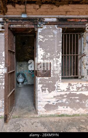 Gefängniszelle mit offener Tür, die die Toilette und das Waschbecken im Inneren zeigt. Stockfoto