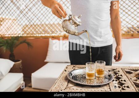 Mann hält in der Hand Silber vintage Teekanne und Gießen traditionelle Minze süßen marokkanischen Tee. Arabische Gastfreundschaft und Service. Stockfoto