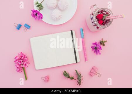 Schmackhafter Smoothie mit Strohhalmen, Marshmallow, Tagebuch, Stift und rosa Blüten auf rosa. Flach liegend. Draufsicht Stockfoto