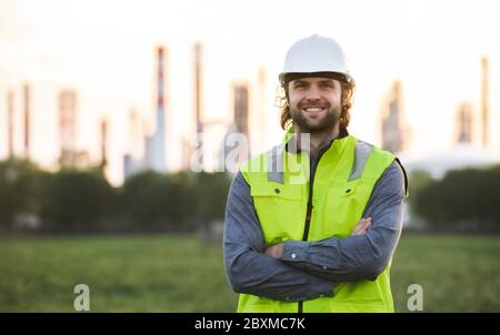 Junger Ingenieur, der draußen bei der Ölraffinerie steht und die Kamera anschaut. Stockfoto