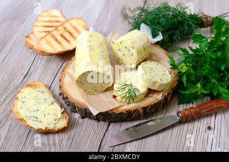 Butter mit einem Kraut für Sandwiches und Steak. Teil der Kräuterbutter auf einem Holzbrett geschnitten. Hausgemachte italienische Küche. Stockfoto