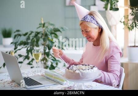 Ältere Frau mit Laptop im Haus, um den Ferngeburtstag zu feiern. Stockfoto