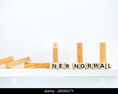 Konzept der sozialen Distanzierung. Reihe von fallenden und stehenden Holzdominos mit Abstand Raum und New Normal, Wörter auf Holz Alphabet Würfel auf weißem Rücken Stockfoto