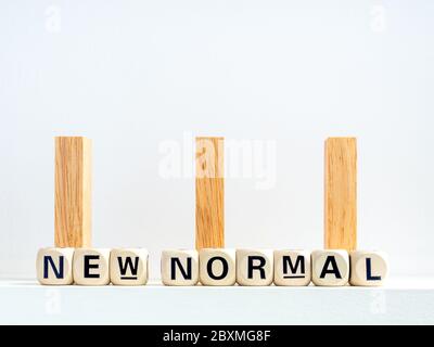 Konzept der sozialen Distanzierung. Reihe von hölzernen Dominosteine mit Abstand Raum und New Normal, Wörter auf hölzernen Alphabet Würfel auf weißem Hintergrund. Stockfoto