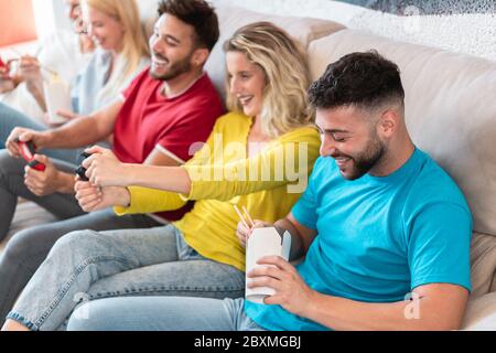 Junge Menschen spielen Konsole Spiel beim Essen Lieferung asiatische Lebensmittel zu Hause - Happy Millennial Freunde Spaß am Haus Wochenende Party - Technologie A Stockfoto