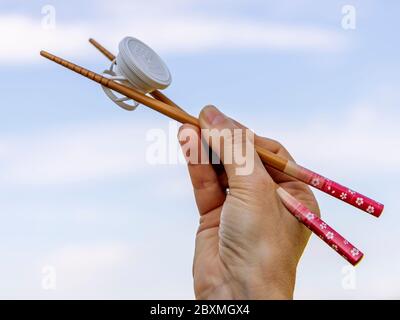 Eine weibliche Hand hält zwei japanische Essstäbchen, mit denen sie ein Stück Plastik hebt, um das Umweltproblem zu symbolisieren Stockfoto