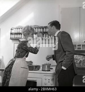 In der Küche 1950er. Ein junges Paar in der Küche. Sie lässt ihn das Essen schmecken und legt ihm einen Löffel in den Mund. Schweden 1959 Kristoffersson Ref. CG35 Stockfoto