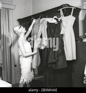 Kleidung der 1920er Jahre. Eine Frau in den 1960er Jahren mit einem Gefühl für die Mode der 1920er Jahre hat verschiedene Outfits auf Kleiderbügeln aus ihrer Garderobe ausgewählt zu tragen. Schweden 1962. Kristoffersson Ref. CS101-10 Stockfoto