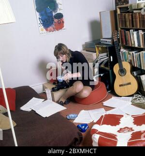 In den 1960er Jahren. Eine junge Frau in ihrer Wohnung. Ein Student zu Hause mit einem Bücherregal voller Bücher und Literatur. Während sie am Telefon telefoniert und eine Zigarette raucht, schaut sie sich einige Dokumente an, die auf dem Boden und dem Bett verteilt sind. Bild aufgenommen im november 21 1968. Kristoffersson Ref. CV51-2 Stockfoto