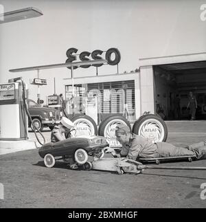 Tankstelle der 1950er Jahre. Ein Junge in seinem Tretauto lässt es an einer Esso-Tankstelle warten. Ein Servicemann hat das kleine Auto angehoben und bedient es. Das Pedalauto wird in Italien von der Firma Giordani hergestellt. Schweden 1958. Kristoffersson Ref. DC100-12 Stockfoto