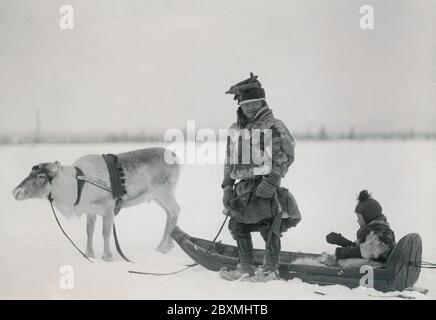 Sami im schwedischen Lappland 1910. Ein Mann mit seinem Rentier, der den traditionellen Schlitten namens ackja zieht, wo sein Kind sitzt. Stockfoto