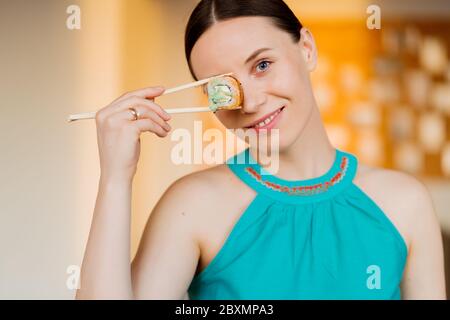 Portrait der schönen Frau, die Sushi-Rolle, gesundes japanisches Essen isst. Schöne Frau hält Essstäbchen mit Sushi über ihren Augen. Stockfoto