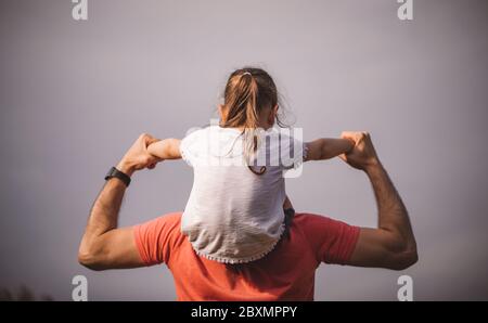 Familienwerte. Vater und Tochter treffen den Sonnenuntergang. Er wird das Mädchen auf seine Schultern legen und ihre Hände halten. Konzept Vatertag. Stockfoto