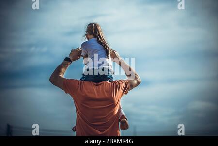 Glückliche Familie Vater und Kind auf Wiese mit einem Drachen im Sommer auf der Natur. Rückansicht des Vaters, der seine kleine Tochter auf den Schultern trägt. Vater Stockfoto