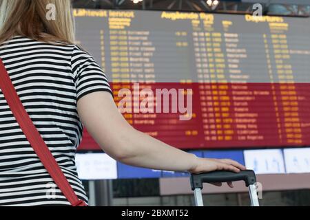 Frau schaut sich die Anzeigetafel am Flughafen an. Wählen Sie ein Land Polen für Reise oder Migration. Stockfoto