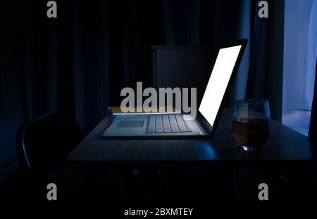 WFH - Überstunden und Arbeit von zu Hause spät in der Nacht auf Laptop mit Notepad und Glas Whisky 1 Stockfoto