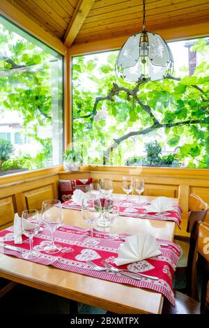 Ein charmanter und einladender Restauranttisch mit Erkerfenster und Weinreben dahinter mit farbenfrohen Platzeinstellungen Stockfoto