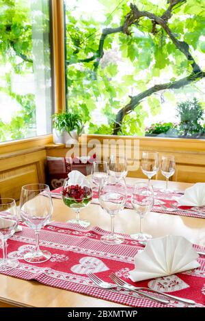 Ein charmanter und einladender Restauranttisch mit Erkerfenster und Weinreben dahinter mit farbenfrohen Platzeinstellungen Stockfoto