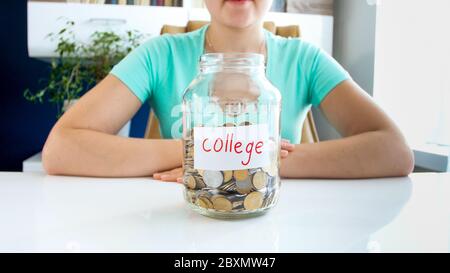 Nahaufnahme Porträt der jungen Dame in T-Shirt sitzt an der weißen Tisch, auf dem befindet, voll von Münzen, Glas mit der Aufschrift Kredit Stockfoto