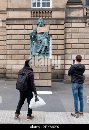 Ein Plakat hängt an der Statue des Philosophen David Hume aus dem 18. Jahrhundert auf der Royal Mile, Edinburgh, nach der Protestkundgebung von Black Lives Matter am 7. Juni 2020 im Holyrood Park, Edinburgh, In Erinnerung an George Floyd, der am 25. Mai in Polizeigewahrsam in der US-Stadt Minneapolis getötet wurde. Stockfoto